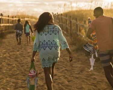 A family of four walks down a sandy path to spend a day on Virginia Beach